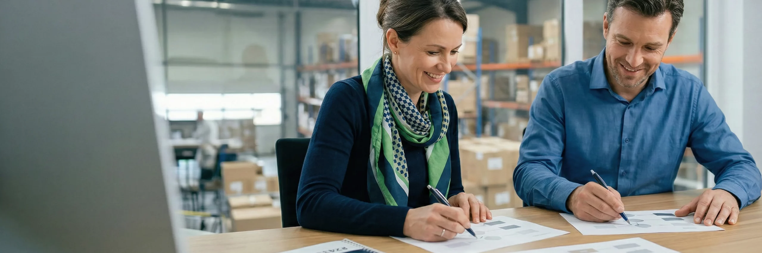 zwei personen mit europaeischem erscheinungsbild sitzen an einem tisch und betrachten diagramm-ausdrucke ohne text; sie markieren werte und laecheln konzentriert, das motiv steht fuer kpis und ursachenanalyse im retourenmanagement